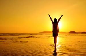 Mulher andando na praia com o pôr do sol, simbolizando liberdade